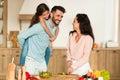 Happy father giving piggyback ride for his daughter while mother cooking vegetarian salad and chatting, kitchen interior Royalty Free Stock Photo