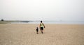 Happy father holding hand of little son walking together on the beach with shoes