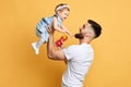 Happy father holding his little kid in hands isolated over yellow background Royalty Free Stock Photo