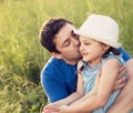 Happy father kissing her laughing daughter in hat on summer green grass background. Closeup portrait of love