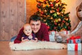 Happy father with little laying on fury carpet in christmas decoration. New year tree on background