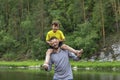 Happy father piggyback his son outside. Laughing boy closed his fathers eyes with his hands