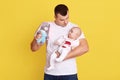 Happy father playing with his baby son or girl with bright rattle, dad holding infant kid and soft toy rabbit in hands, handsome Royalty Free Stock Photo