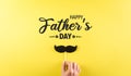 Happy Father`s Day background concept with hand holding black mustache with the text on pastel yellow background