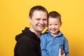 Cute father and son hugging on yellow background. Portrait of a dad with a baby boy smiling and hugging. Family concept Royalty Free Stock Photo