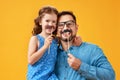 Happy father`s day! funny dad and daughter with mustache fooling around on yellow background Royalty Free Stock Photo