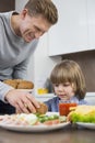 Happy father serving meal to son at table in kitchen Royalty Free Stock Photo