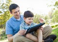 Helpful Father and Son Playing on a Computer Tablet Outside. Royalty Free Stock Photo