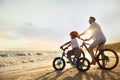 Happy father with son riding bicycles on sandy beach near sea at sunset Royalty Free Stock Photo