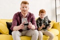 happy father and son sitting on sofa and playing with joysticks Royalty Free Stock Photo