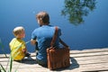 Happy father and son sitting on wooden pier near lake on summy summer day. Dad and child boy spend time together on wharf Royalty Free Stock Photo