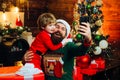 Happy father and son talking with mobile phone near Christmas tree. Little Santa and old bearded Santa using smartphone