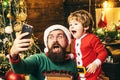 Happy father and son talking with mobile phone near Christmas tree. Little Santa and old bearded Santa using smartphone. Royalty Free Stock Photo