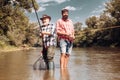 Happy father and son together fishing in summer day under beautiful sky on the river. Fisherman and trophy trout. Still Royalty Free Stock Photo