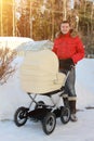 happy father stands with pram with sleeping child in backyard with snowdrifts on winter sunny day. Man in red jacket looks into Royalty Free Stock Photo