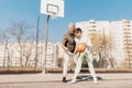 Happy father and teenage daughter playing basketball outside at court.