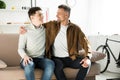 Happy father and teen son hugging on sofa at home, looking Royalty Free Stock Photo