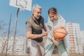 Happy father and teenage daughter playing basketball outside at court.