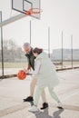 Happy father and teenage daughter playing basketball outside at court.