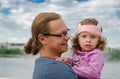 A happy father with a two-year-old daughter in his arms. A girl in a pink blouse, in the background there is a river Royalty Free Stock Photo