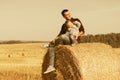 Happy father and two year old girl sitting on hay bale in harvested field