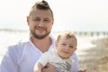 Happy father on vacation - smiling man standing on a beach holding his little baby son