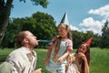 Happy father wearing party hat, blowing whistle together with kids, celebrating birthday in the park on a summer day Royalty Free Stock Photo