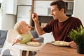 Side view of dad feeding baby holding fork with spaghetti during lunch time at kitchen table