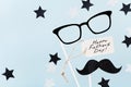 Happy Fathers Day background with greeting tag, glasses, funny moustache and star confetti on table top view. Flat lay style.