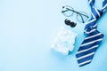 Happy fathers day concept. Top view of blue tie, beautiful gift box, glasses and mustache on bright blue pastel background. Flat