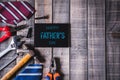 Happy fathers day concept. Top view of white picture frame with border of tools and ties, retro film camera on dark wooden table Royalty Free Stock Photo