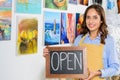 happy female artist holding signboard with word open