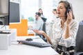 Happy female call center operator in headset making video call to business partner using computer in office. Royalty Free Stock Photo