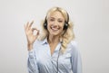 Happy female call centre operator with headset showing okay gesture and smiling at camera on light studio background Royalty Free Stock Photo