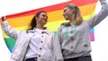 Happy female couple raising rainbow flag, march for LGBT rights, same sex love