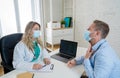 Happy female doctor and patient wearing protective face mask having a consultation in clinic office Royalty Free Stock Photo