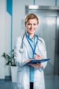 happy female doctor with stethoscope over neck writing in clipboard and looking at camera Royalty Free Stock Photo