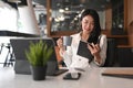 Happy female entrepreneur wearing earphone drinking coffee and reading book at workplace.