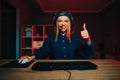 Happy female gamer in headset sitting at computer desk at home with smile on face, looking at camera and showing thumbs up. Lady