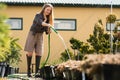 Happy female garden center worker watering plant pots with a hose.