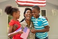 Happy female mid adult african american soldier embracing son and daughter holding american flags Royalty Free Stock Photo