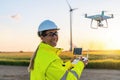 Happy Female Operator inspecting Wind turbine with drone at sunset. Drone inspection concept image. renewable energy wind park in