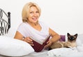 Happy female pensioner with cat reading book Royalty Free Stock Photo