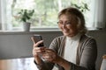 Happy female pensioner holding mobile phone enjoy using web app