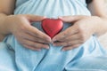 Happy female pregnancy. Pregnant woman in blue dress holding red heart sign over tummy