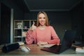 Happy female student sits at a desk at home near a laptop and with a smile on her face, studies remotely and shows a thumbs up Royalty Free Stock Photo