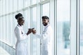 Happy african female surgeon holding coffee mug while looking at indian coworker in hospital Royalty Free Stock Photo