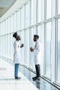 Happy african female surgeon holding coffee mug while looking at indian coworker in hospital Royalty Free Stock Photo