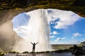 Happy female traveler feeling the power of Seljalandsfoss waterfall in the South of Iceland, person standing behind the stream,