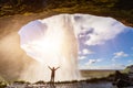 Happy female traveler feeling the power of Seljalandsfoss waterfall in the South of Iceland, person standing behind the stream, Royalty Free Stock Photo